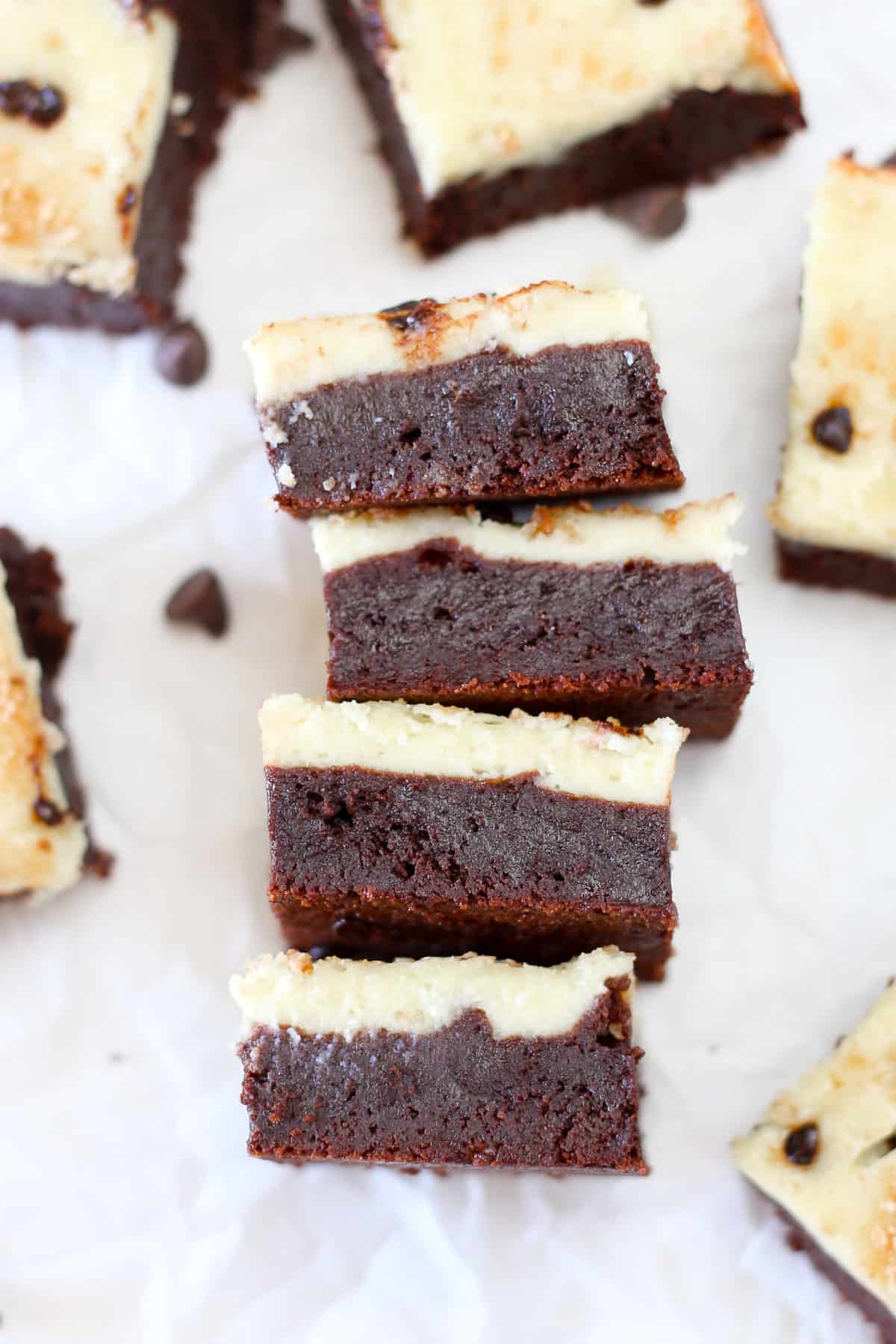 Four chocolate chip cheesecake brownies on their side sowing the distinct brownie and cheesecake layers.
