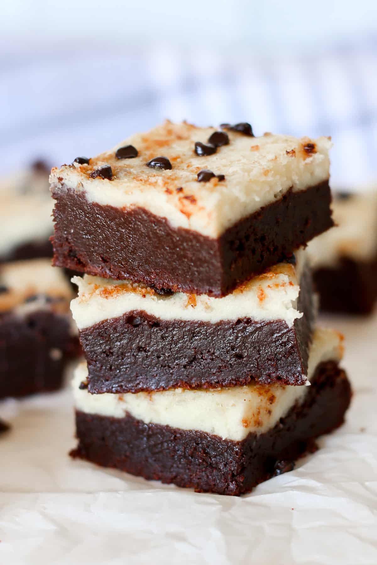 Three chocolate chip cheesecake brownies stacked up showing the distinct layers of brownie and cheesecake.