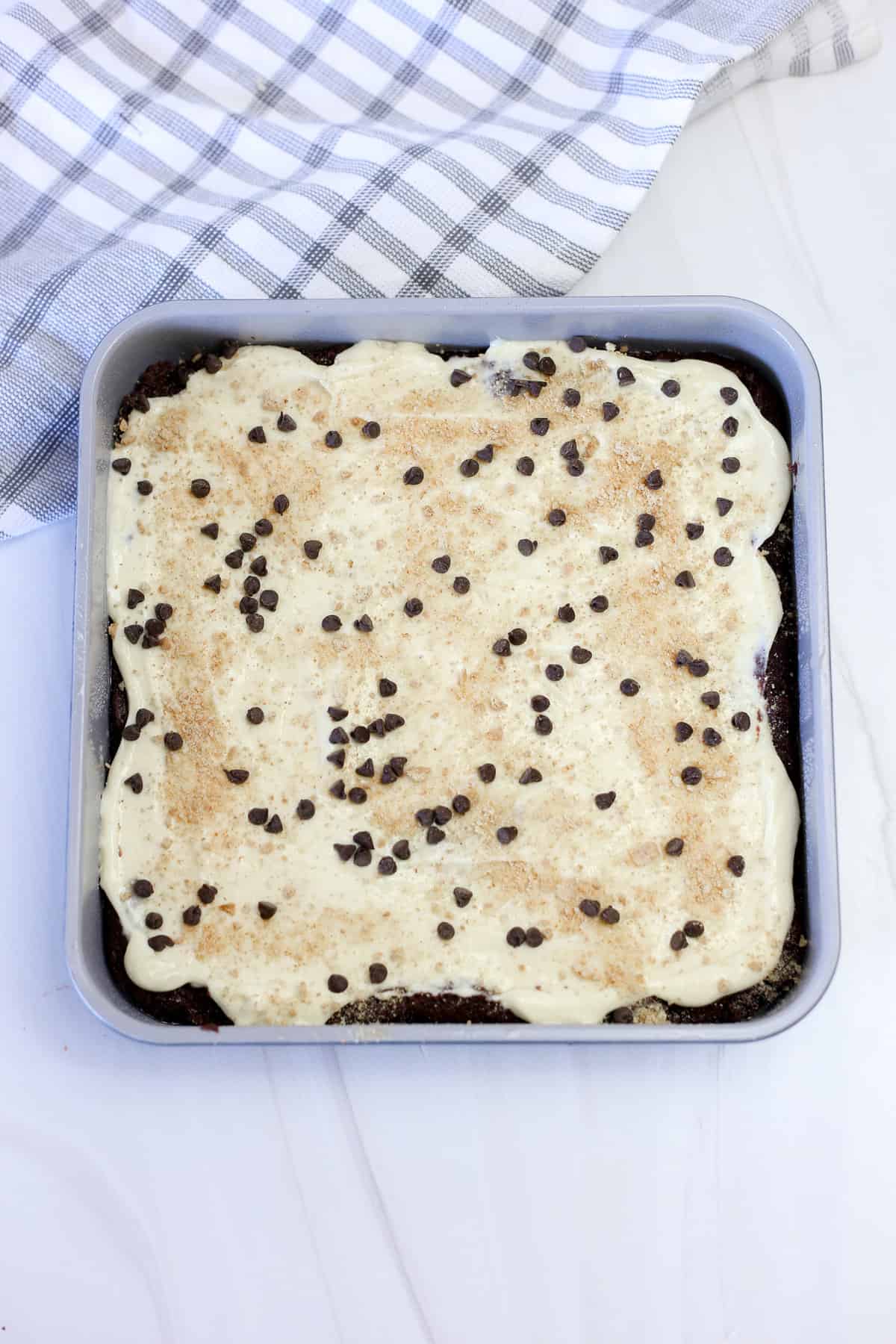 Brownies baked in a square pan with a cheesecake layer topped with graham cracker crumbs and mini chocolate chips.