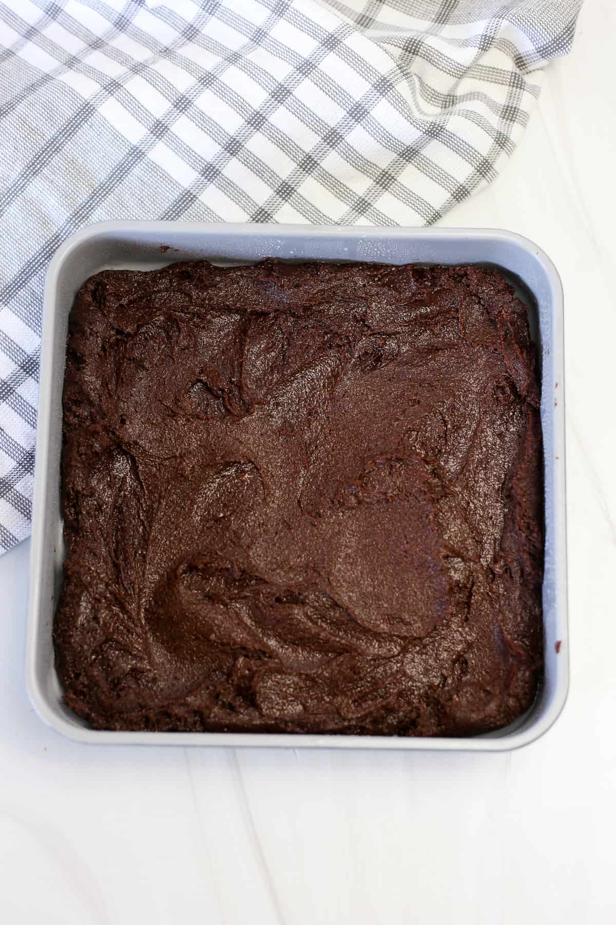 Brownie batter spread in a square metal pan before being baked.