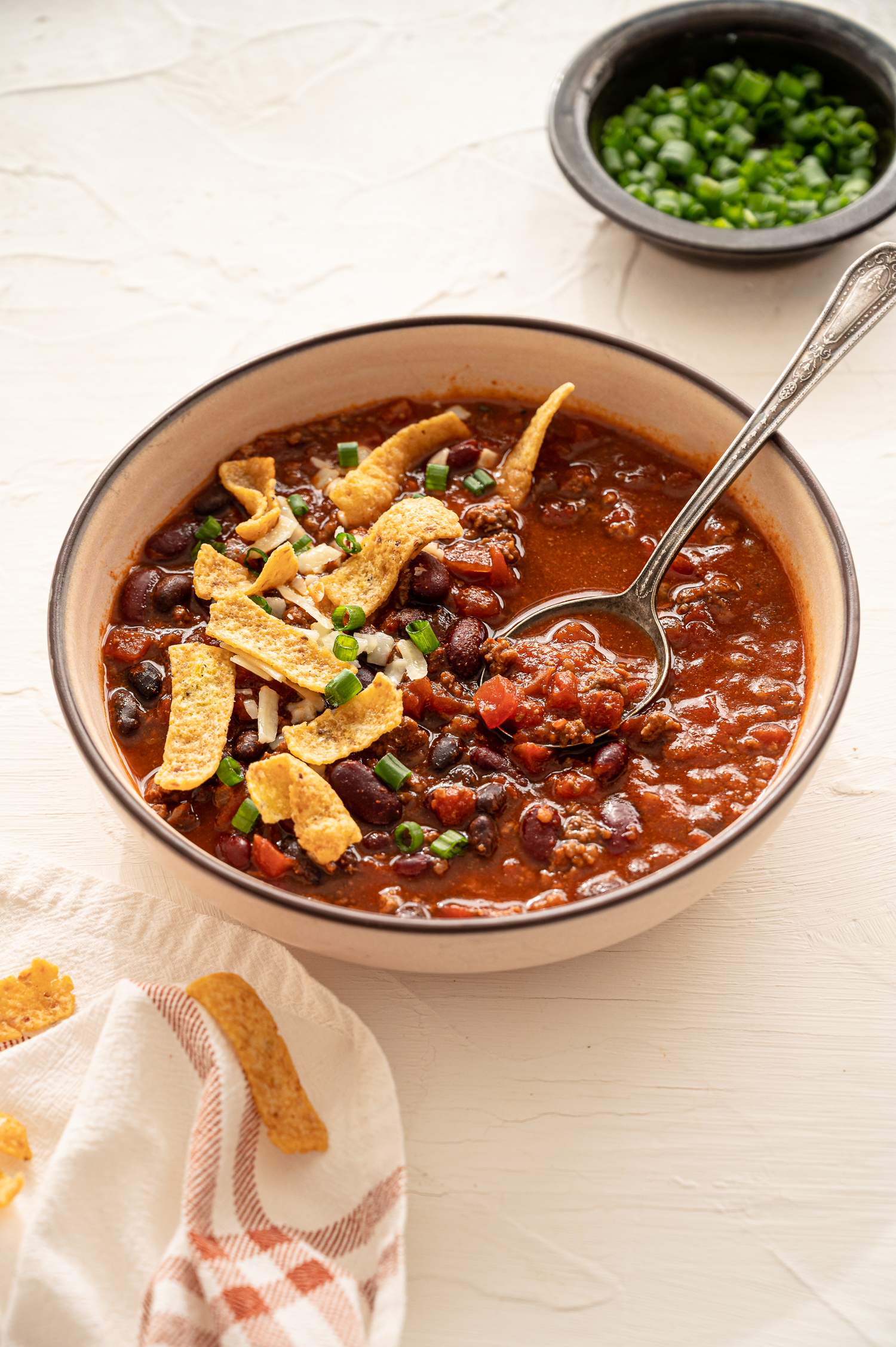 A bowl of chili with a spoon topped with fritos chips.