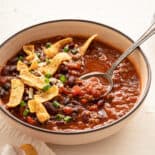 A bowl of chili with a spoon topped with fritos chips.