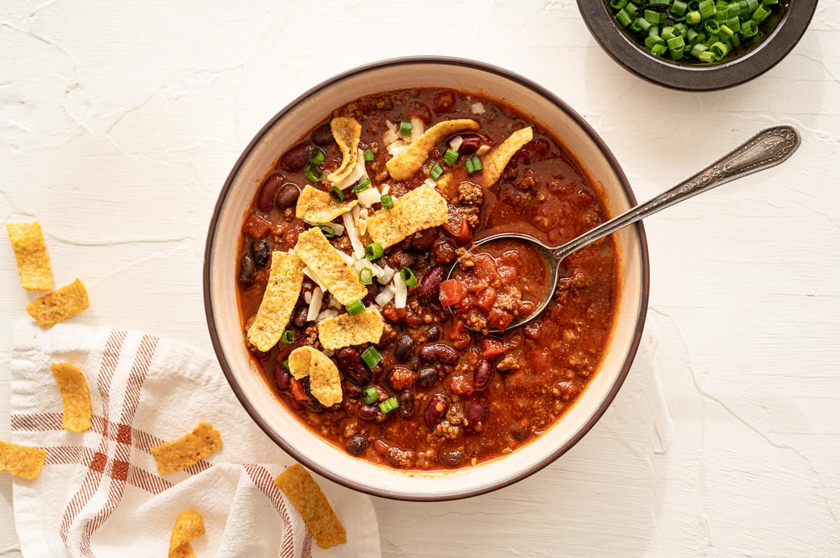 A bowl of chili with a spoon topped with fritos chips.