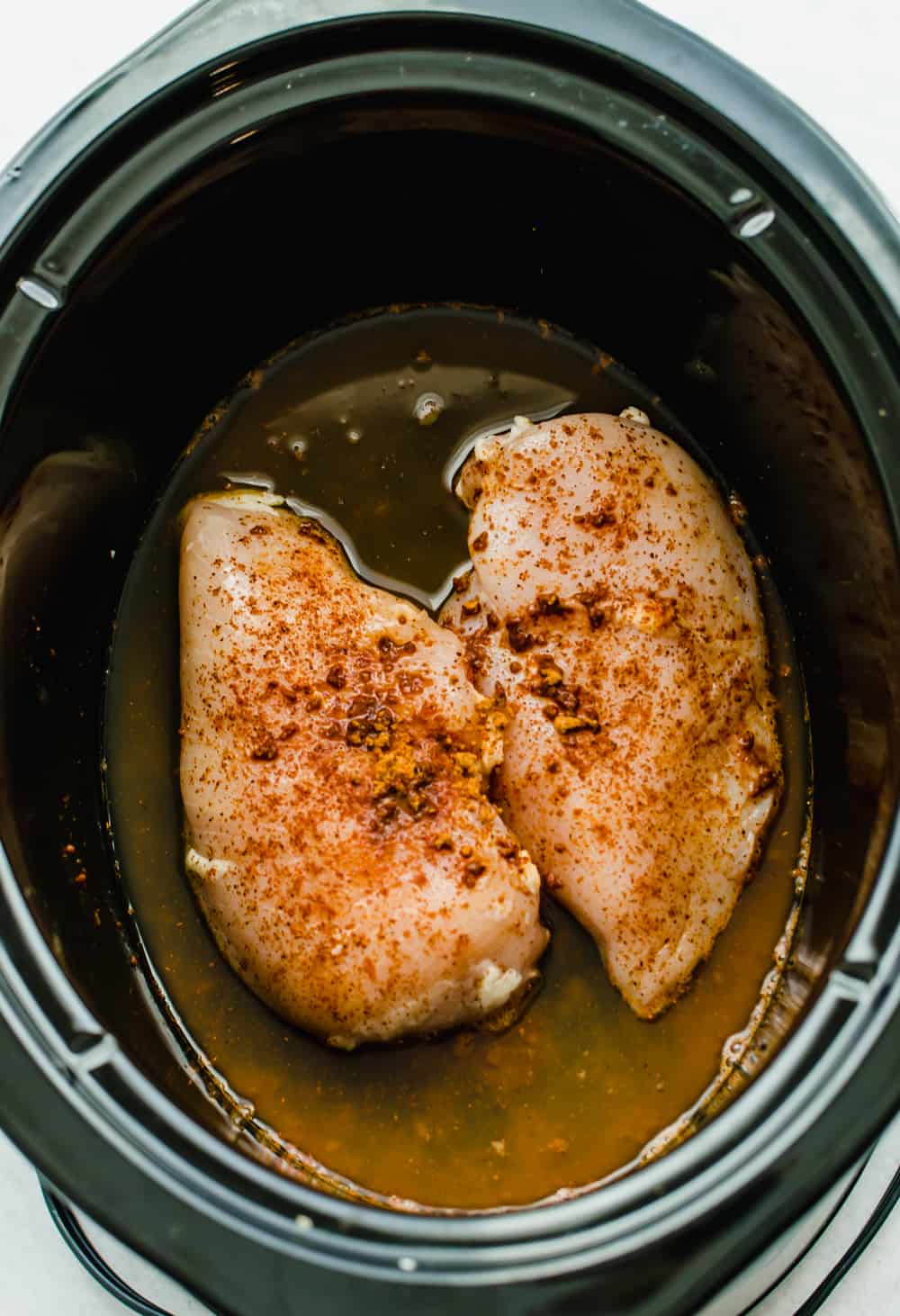 Two raw chicken breasts seasoned with taco seasoning in the crock pot.