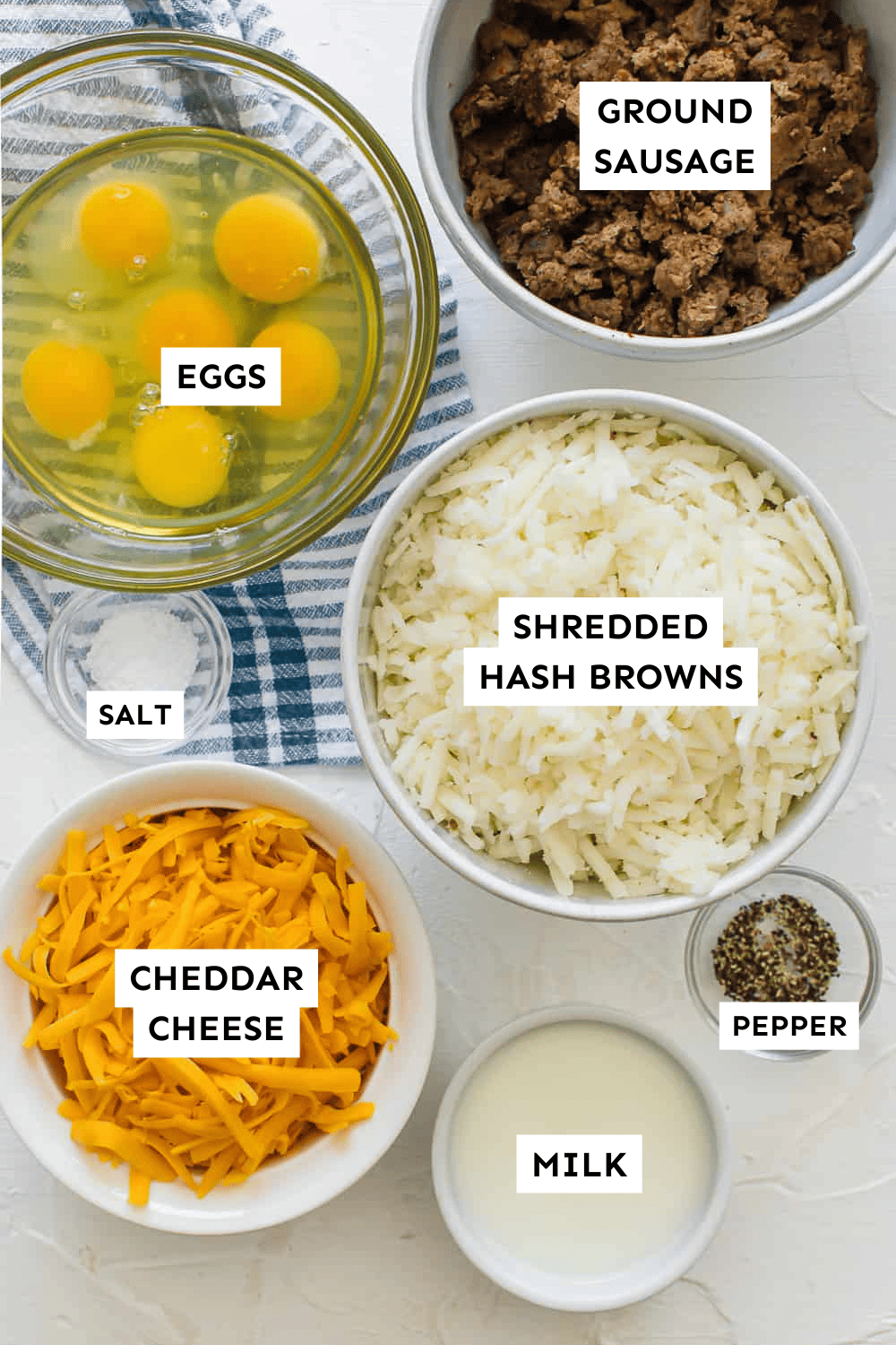 Ingredients in bowls for a make ahead breakfast casserole, including hash browns, sausage, cheese, eggs, milk, and salt and pepper.