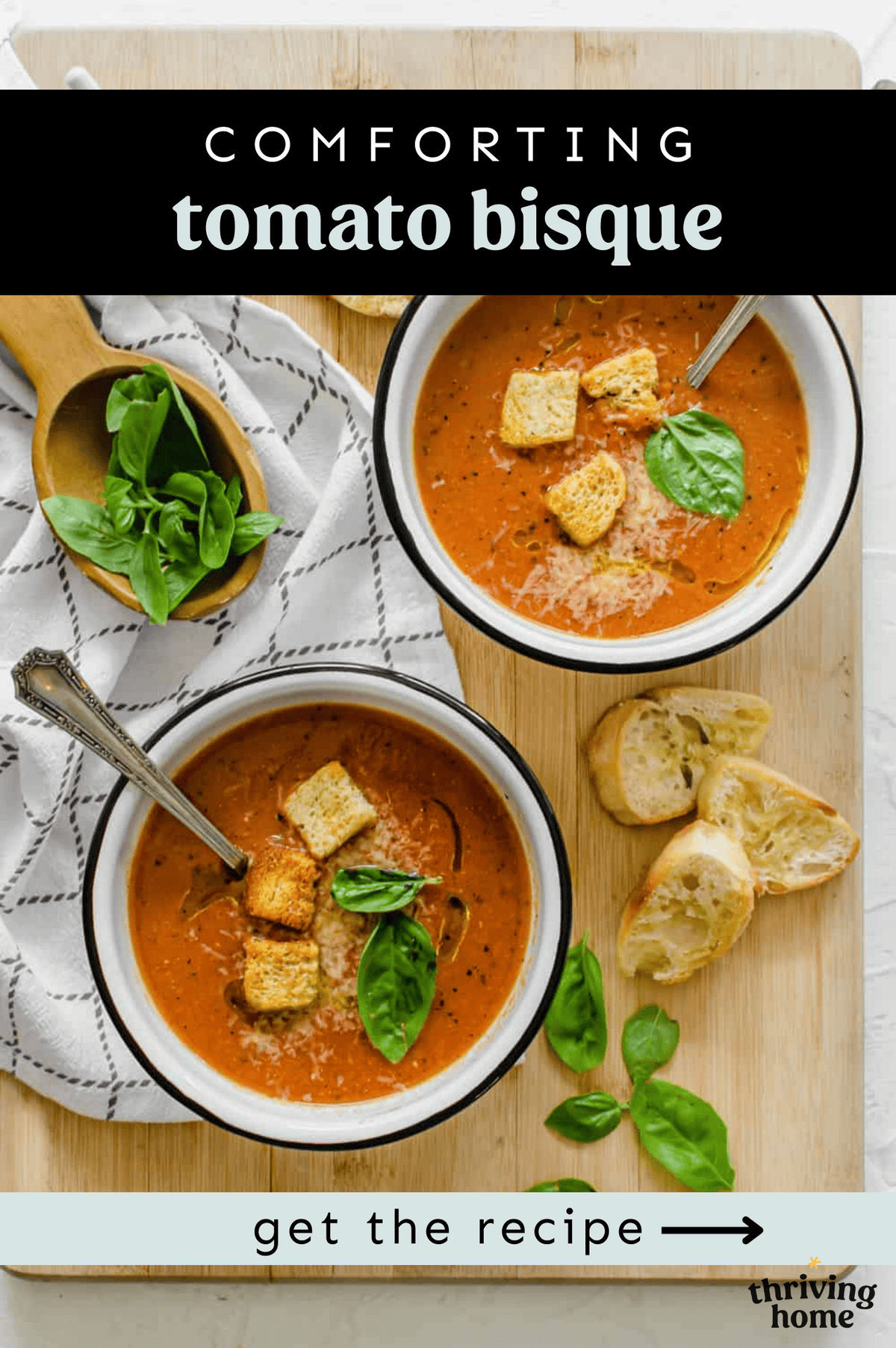 Two bowls of tomato bisque  with crusty bread and fresh basil next to them.