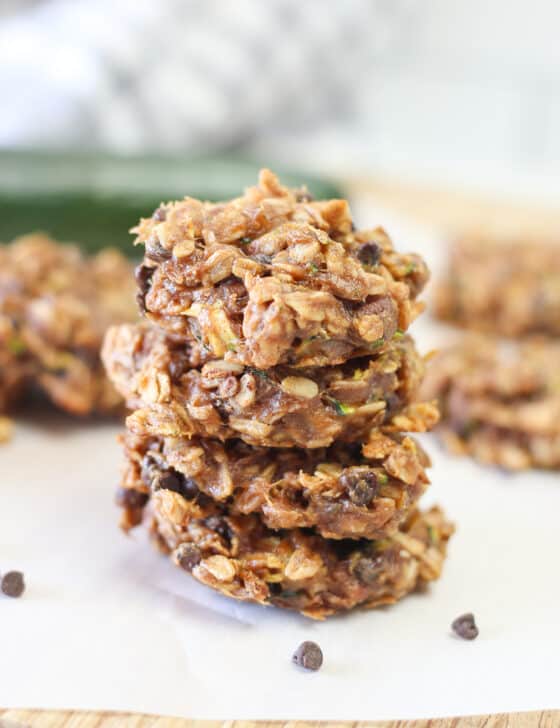Three zucchini breakfast cookies stacked up on parchment paper with mini chocolate chips sprinkled around.