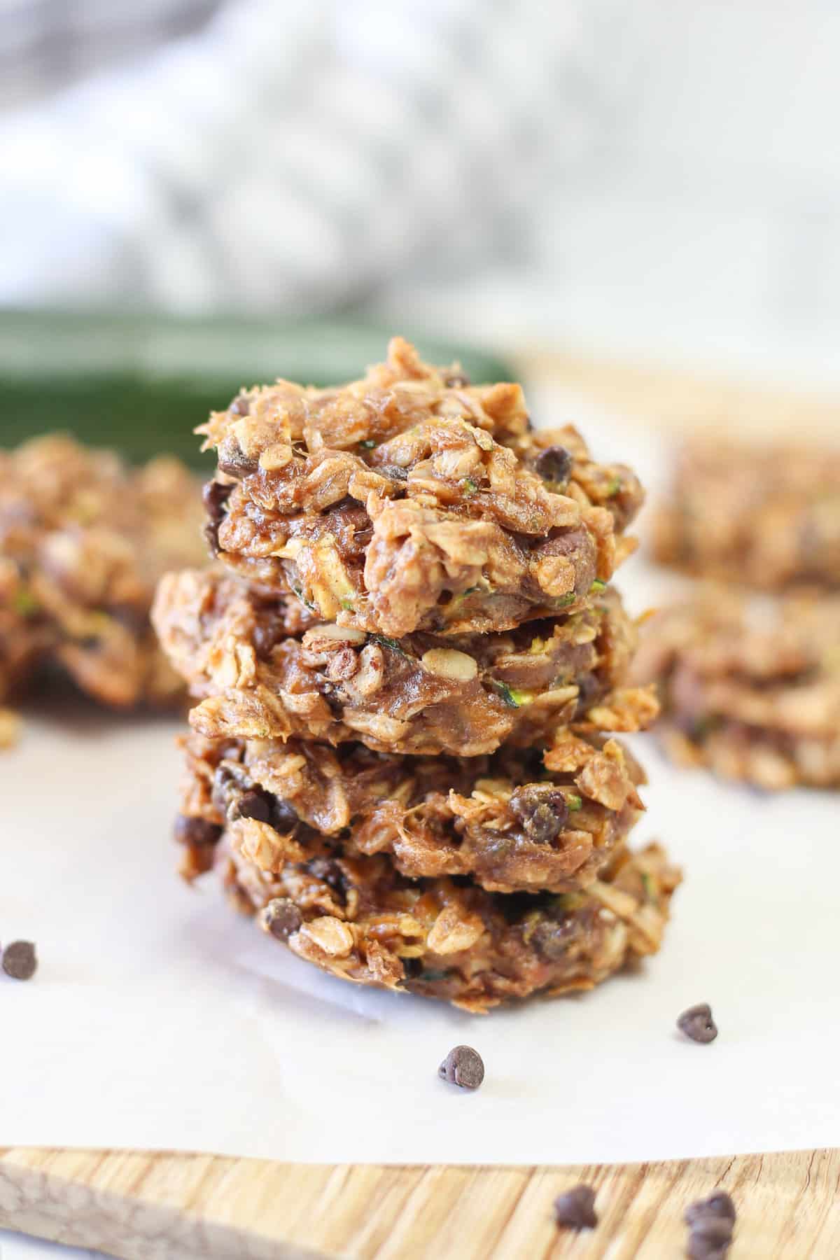 Three zucchini breakfast cookies stacked up on parchment paper with mini chocolate chips sprinkled around.