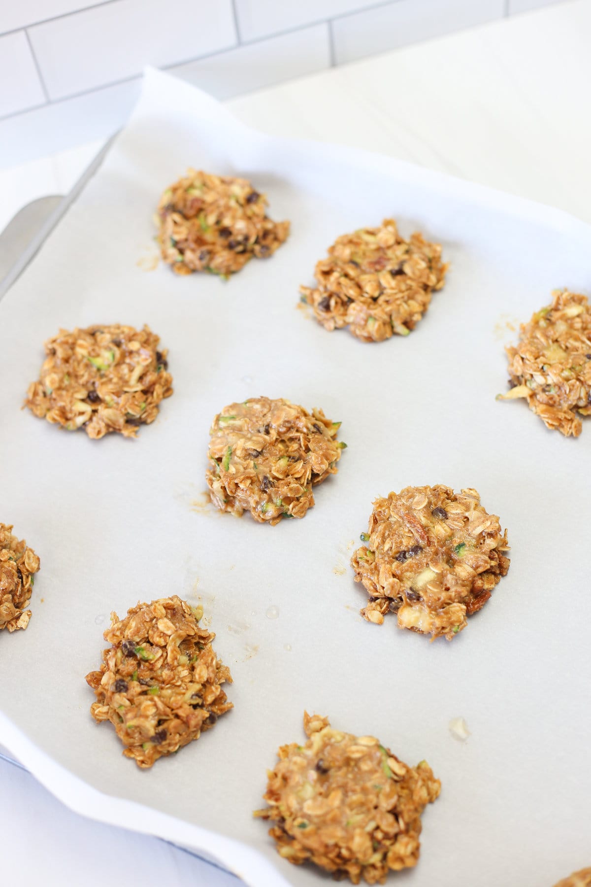 Zucchini breakfast cookies lined up on parchment paper prior to baking.