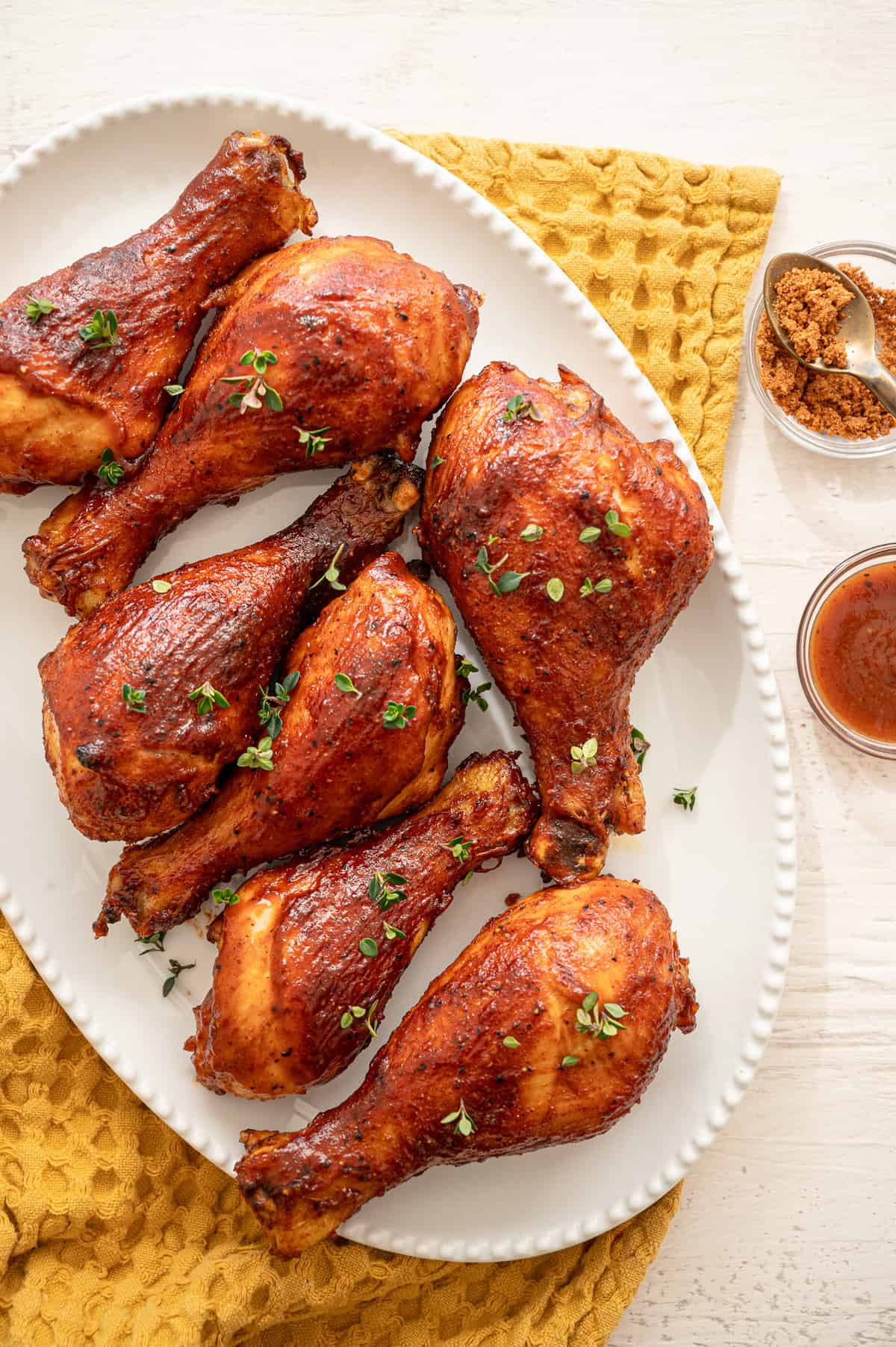 BBQ chicken drumsticks lined up on a white platter with fresh thyme sprinkled on top.
