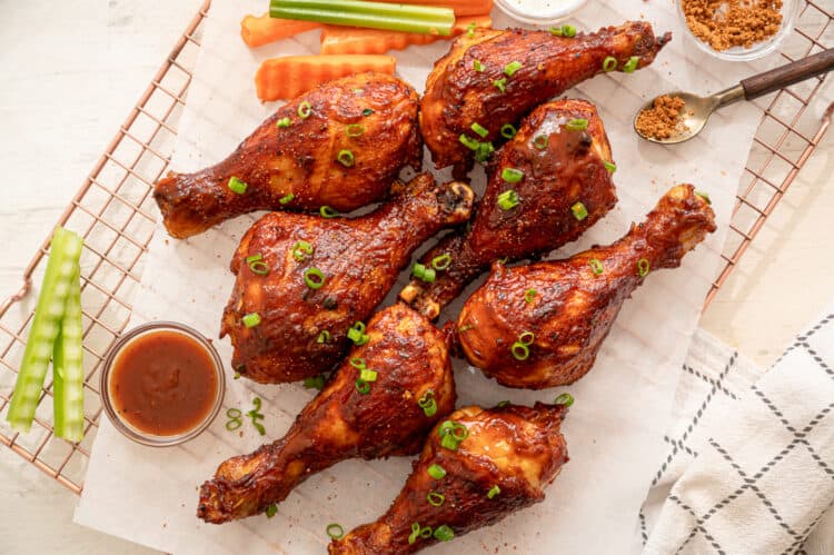 BBQ chicken drumsticks lined on parchment paper served with extra BBQ sauce and crinkle cut celery and carrots.