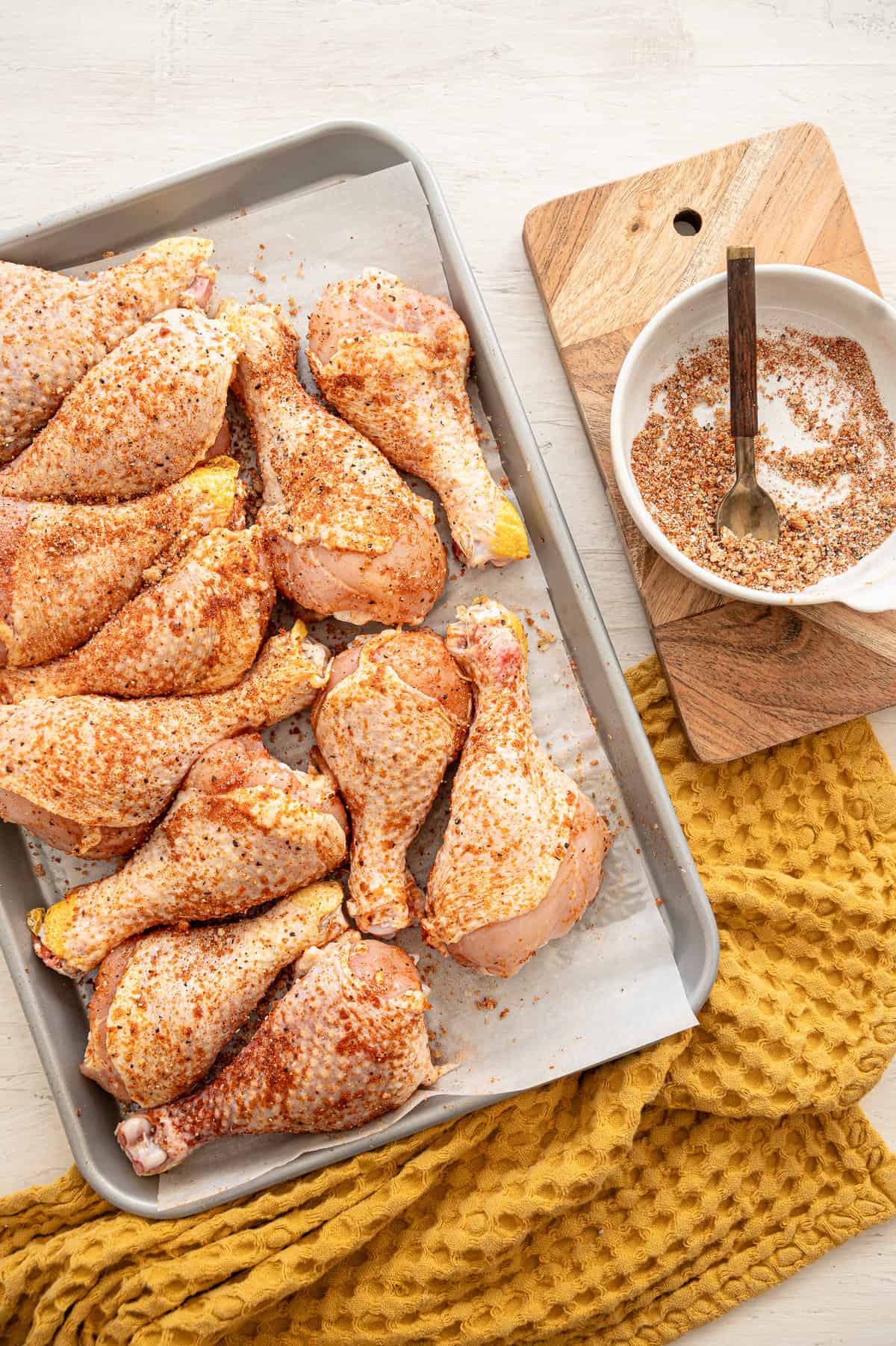 Raw chicken drumsticks with a rub on a baking sheet.