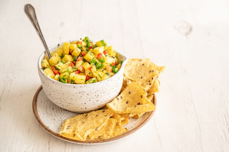 Tortilla chips on the side of a small crock of pineapple salsa.