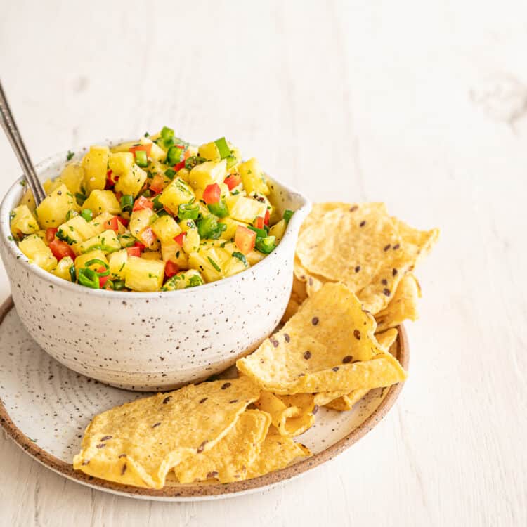 Tortilla chips on the side of a small crock of pineapple salsa.