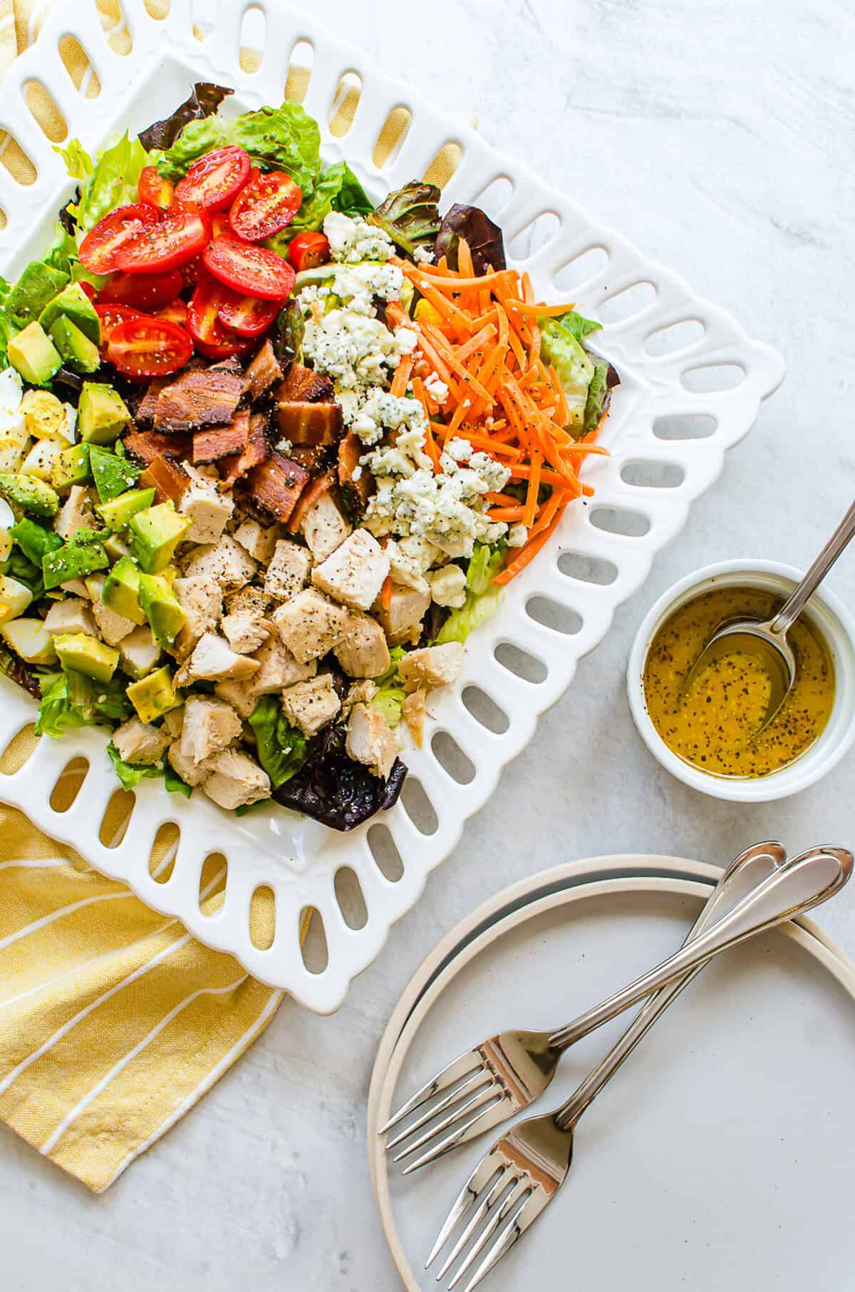 Cobb salad on a white platter with dressing in a bowl. 
