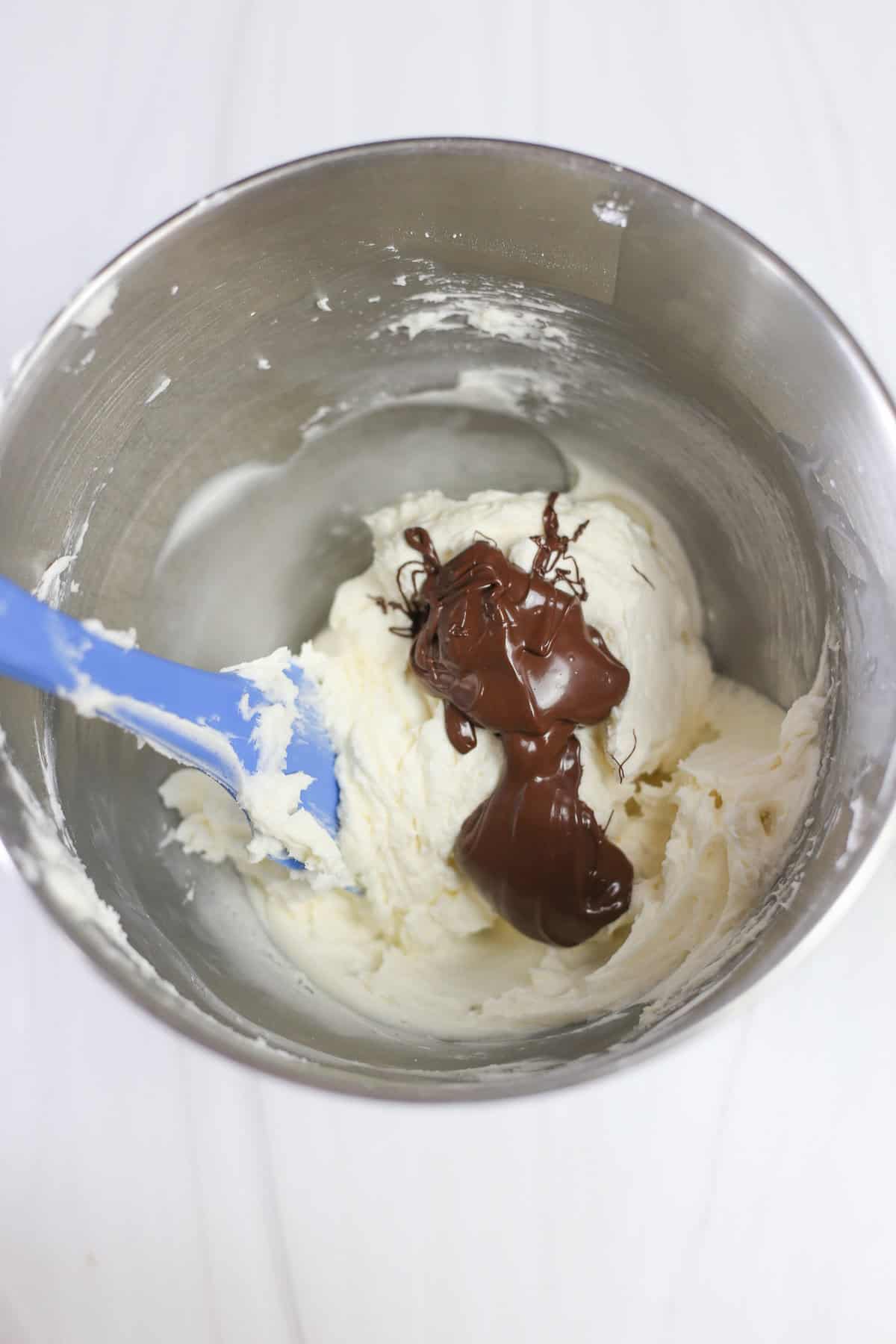 Melted chocolate chips being mixed into buttercream frosting.