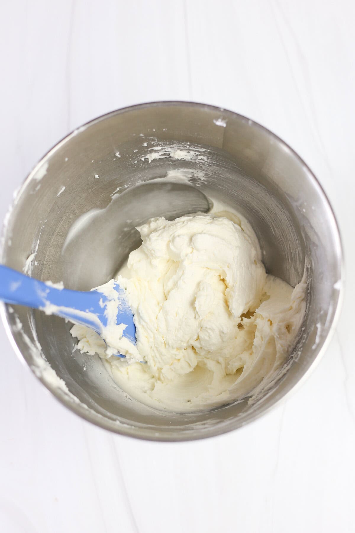 Buttercream frosting in a mixing bowl with a blue spatula.