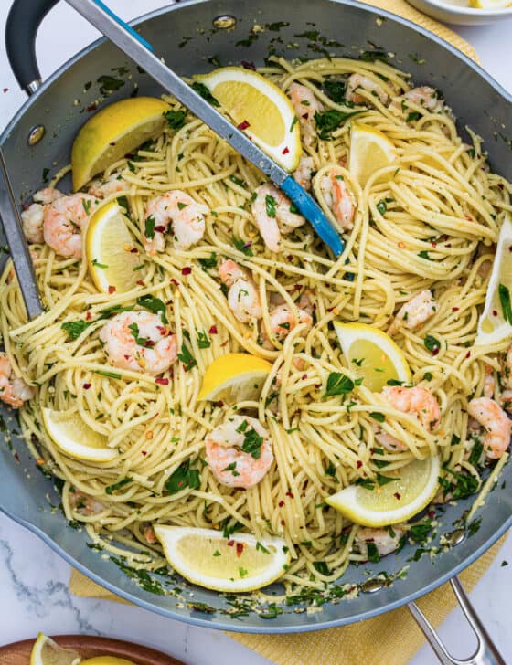 Shrimp Scampi Pasta in a large pan with tongs and lemon slices.
