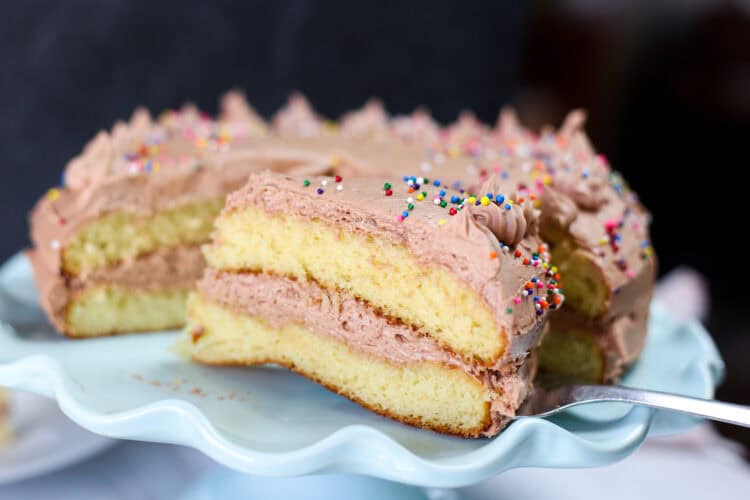 A slice of double layer yellow cake being lifted from the cake stand with a server.