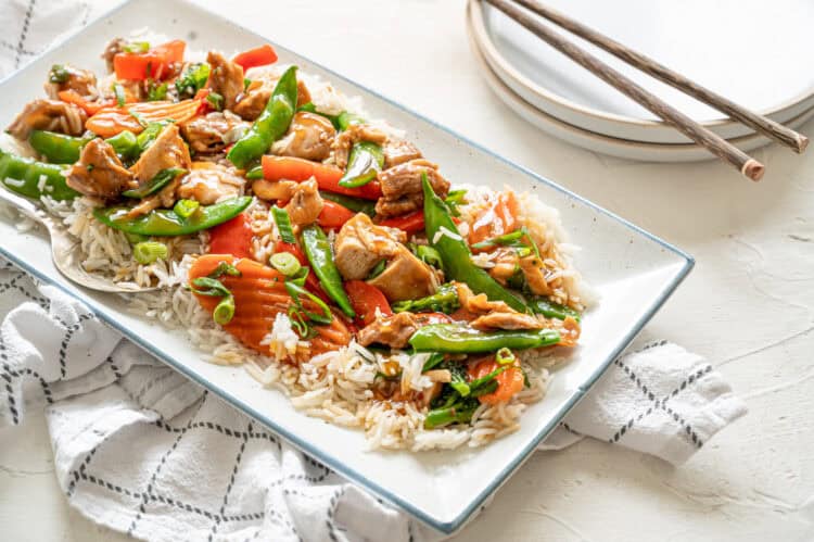 A platter of honey bourbon chicken served on top of rice with stir-fried veggies.