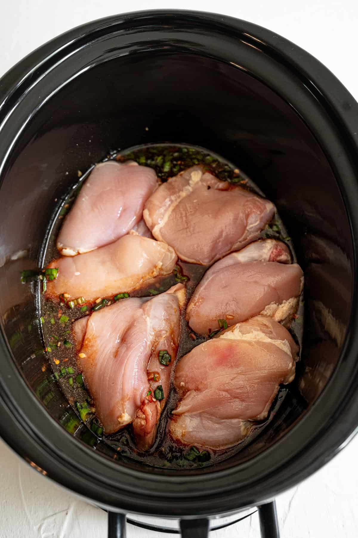 Raw chicken thighs covered with honey bourbon marinade in a crock pot.