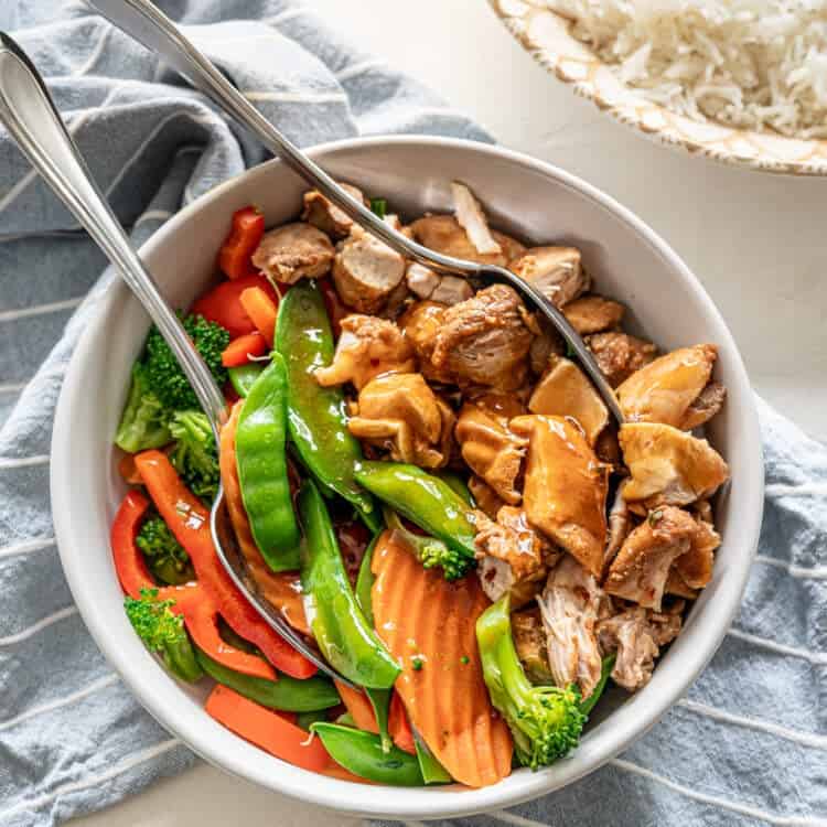 Honey bourbon chicken in a bowl with stir-fry veggies covered in sauce.