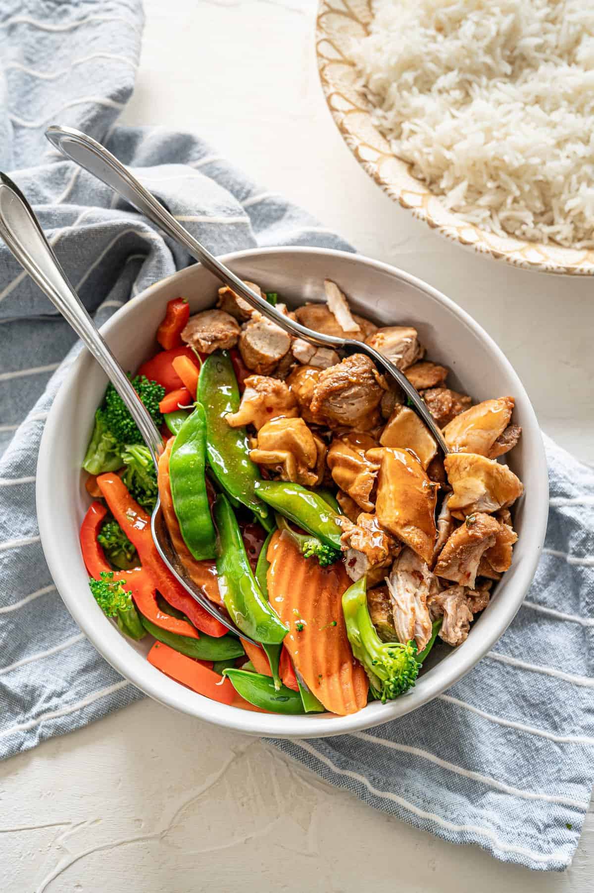 Honey bourbon chicken in a bowl with stir-fry veggies covered in sauce.