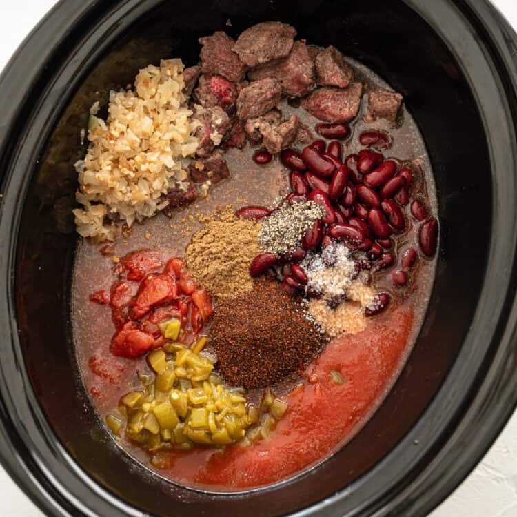 Ingredients for steak chili dumped in a slow cooker.