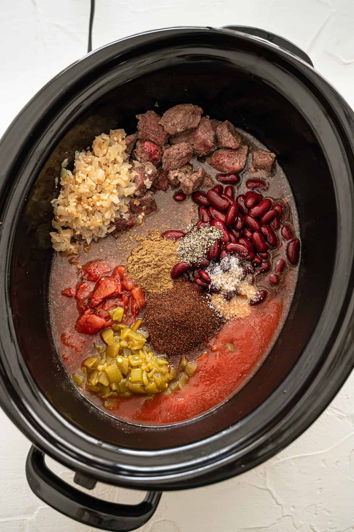 Ingredients for steak chili dumped in a slow cooker.