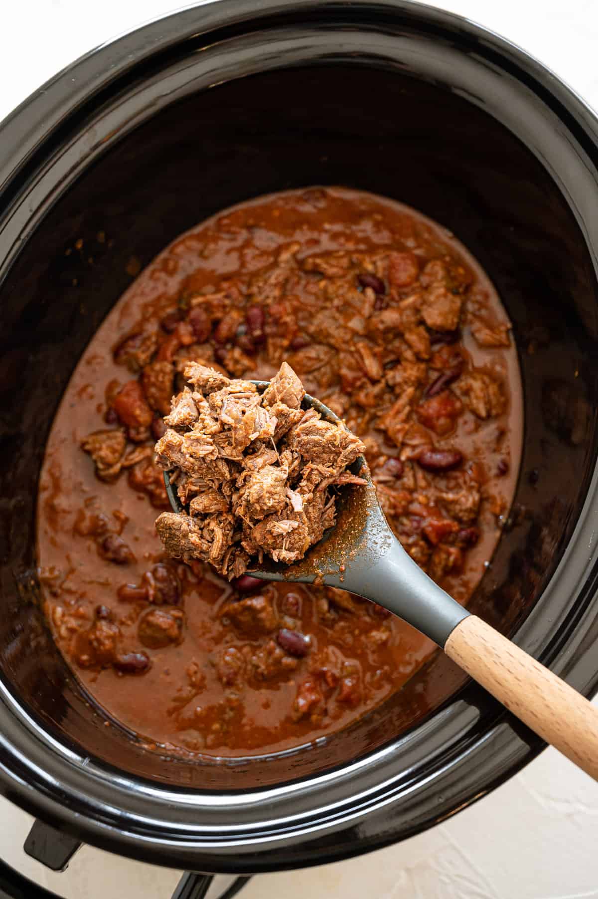 Steak chili being served with a wooden spoon out of a slow cooker.