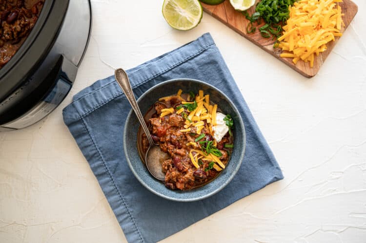 Steak chili in a bowl with a cutting board of toppings to the side.