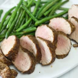 Air fryer pork tenderloin served in slices with green beans.
