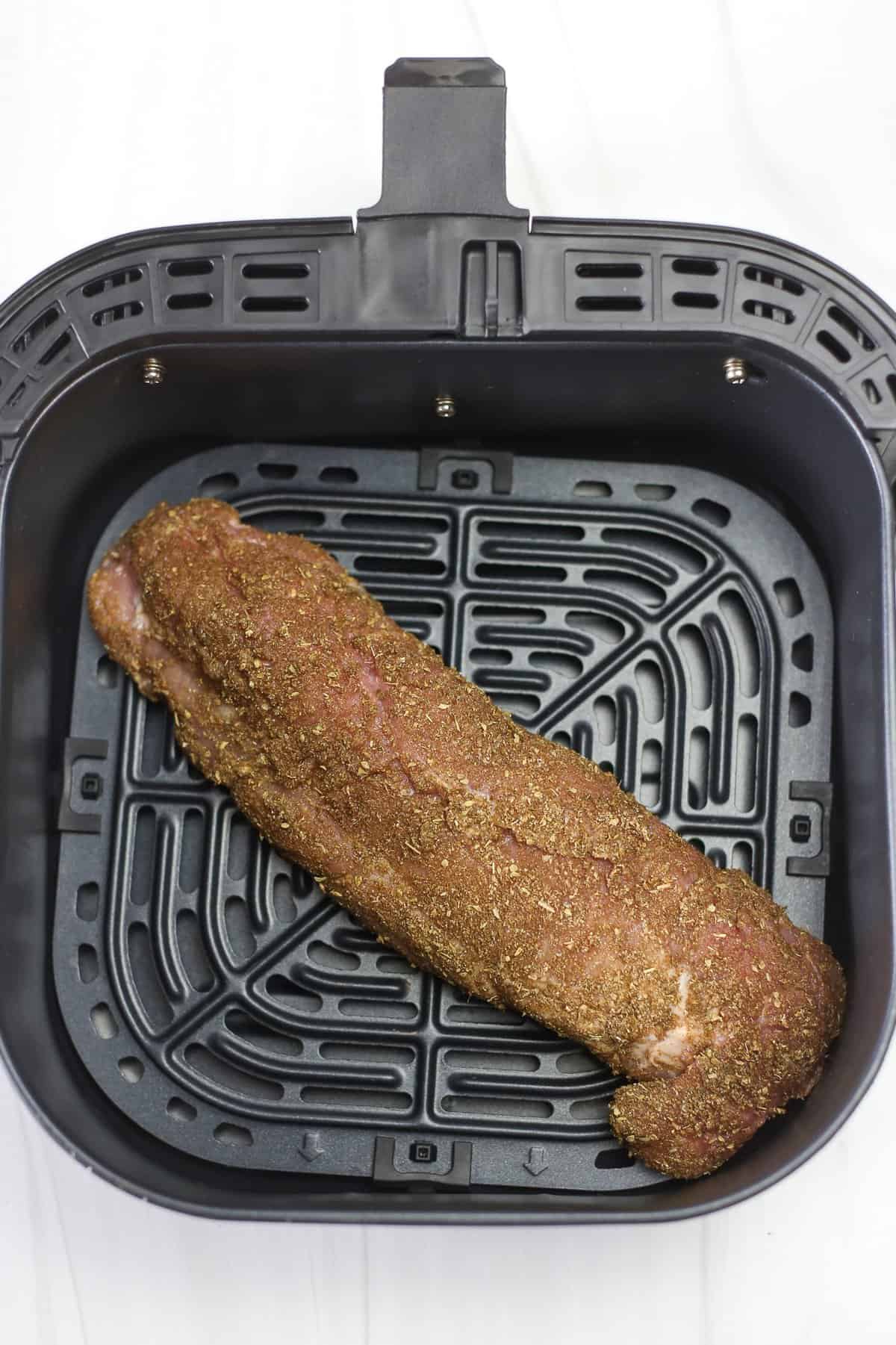 Pork tenderloin with seasoning rub in an air fryer basket ready to be cooked.