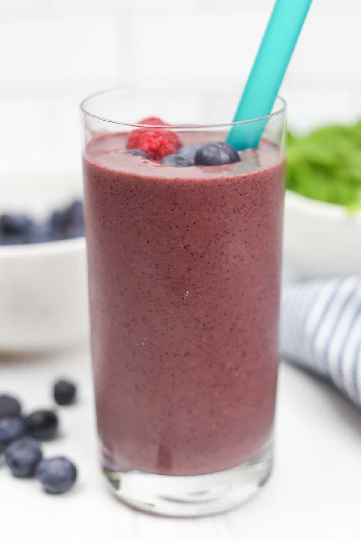 A purple smoothie in a glass cup with berries on top. 