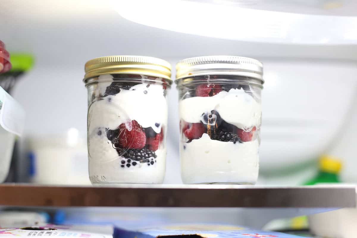 Two fruit and yogurt parfaits in the fridge stored in small mason jars.