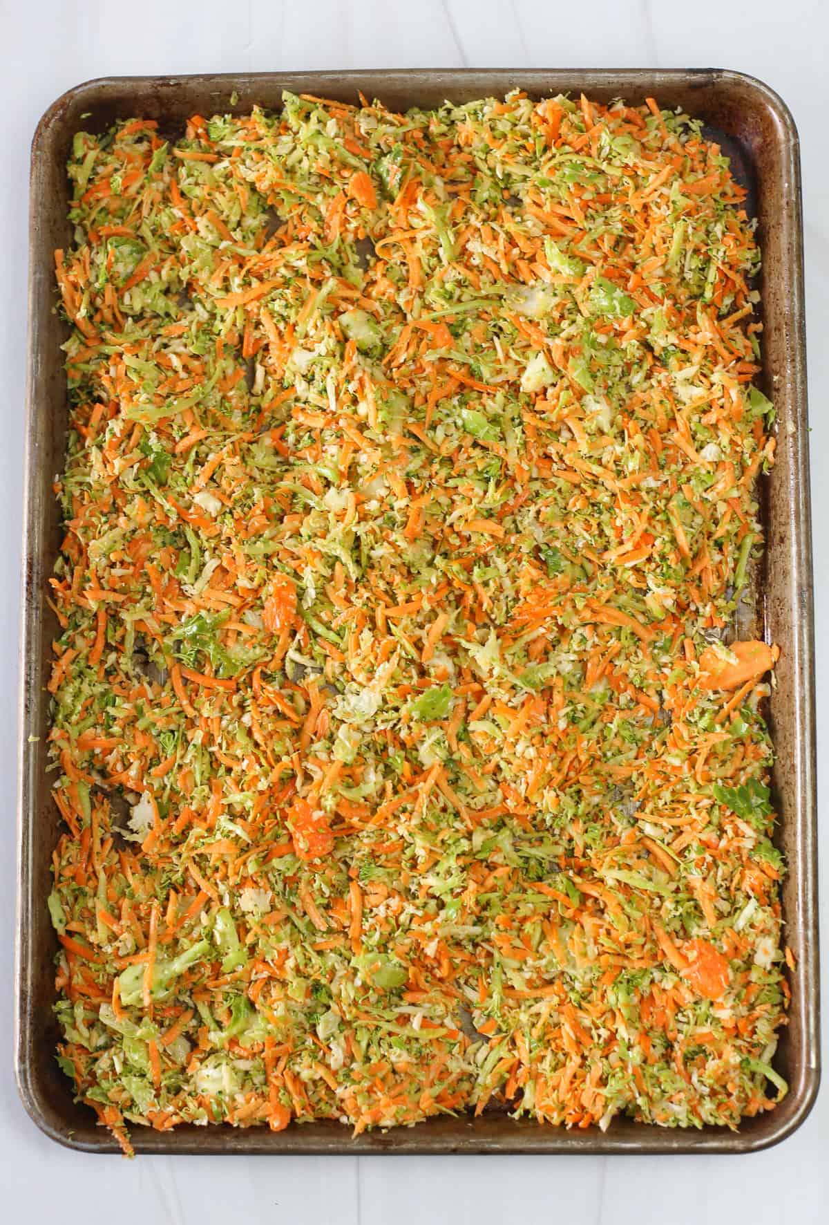 Shredded vegetables spread out on a baking sheet ready to be roasted.
