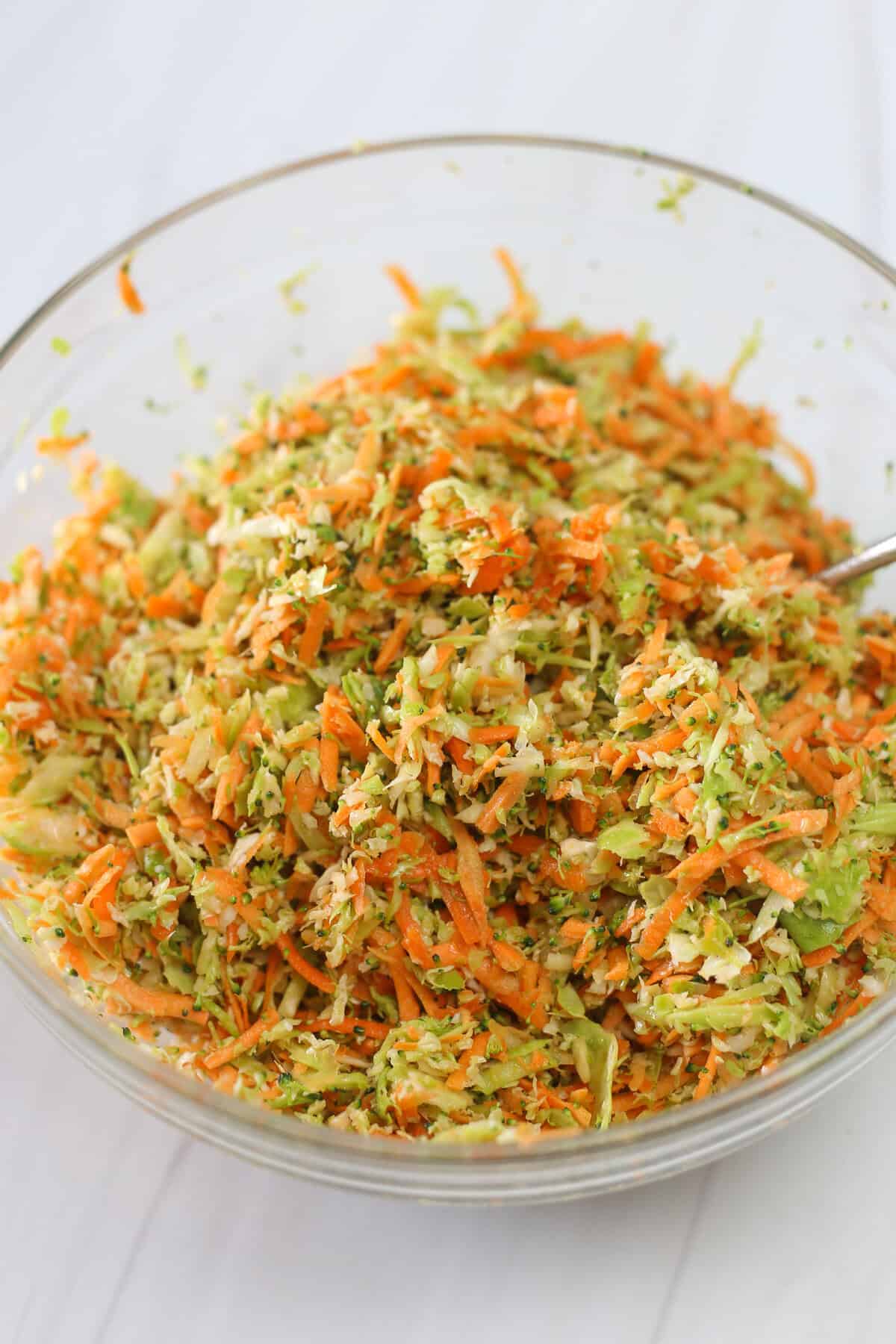 Shredded vegetables in a glass bowl being tossed with olive oil and salt & pepper.