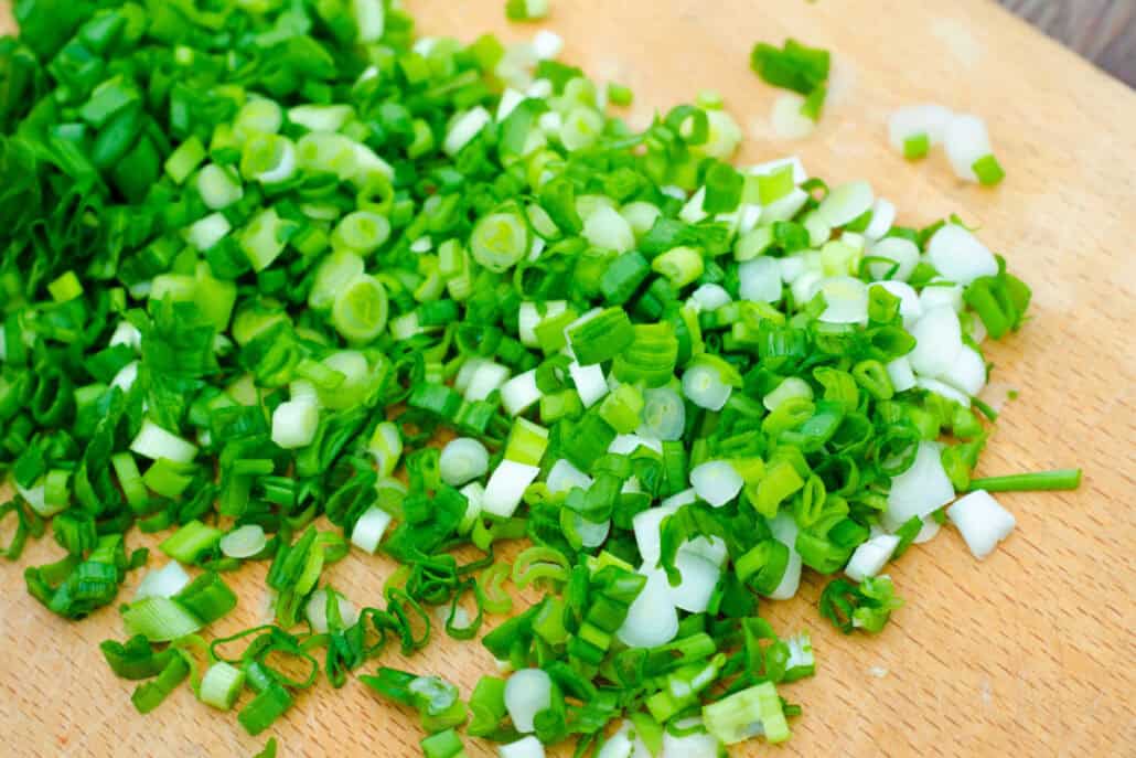 A pile of chopped green onions on a cutting board. 