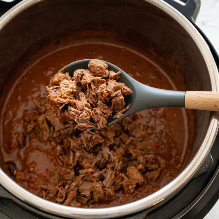 Wooden spoon above an Instant Pot holding shredded beef stew meat to stir into the rest of the Steak Chili ingredients.