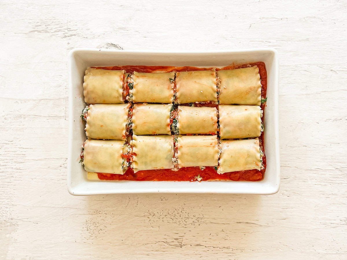 A baking dish with marinara sauce on the bottom and spinach lasagna rolls lined up in rows of three.