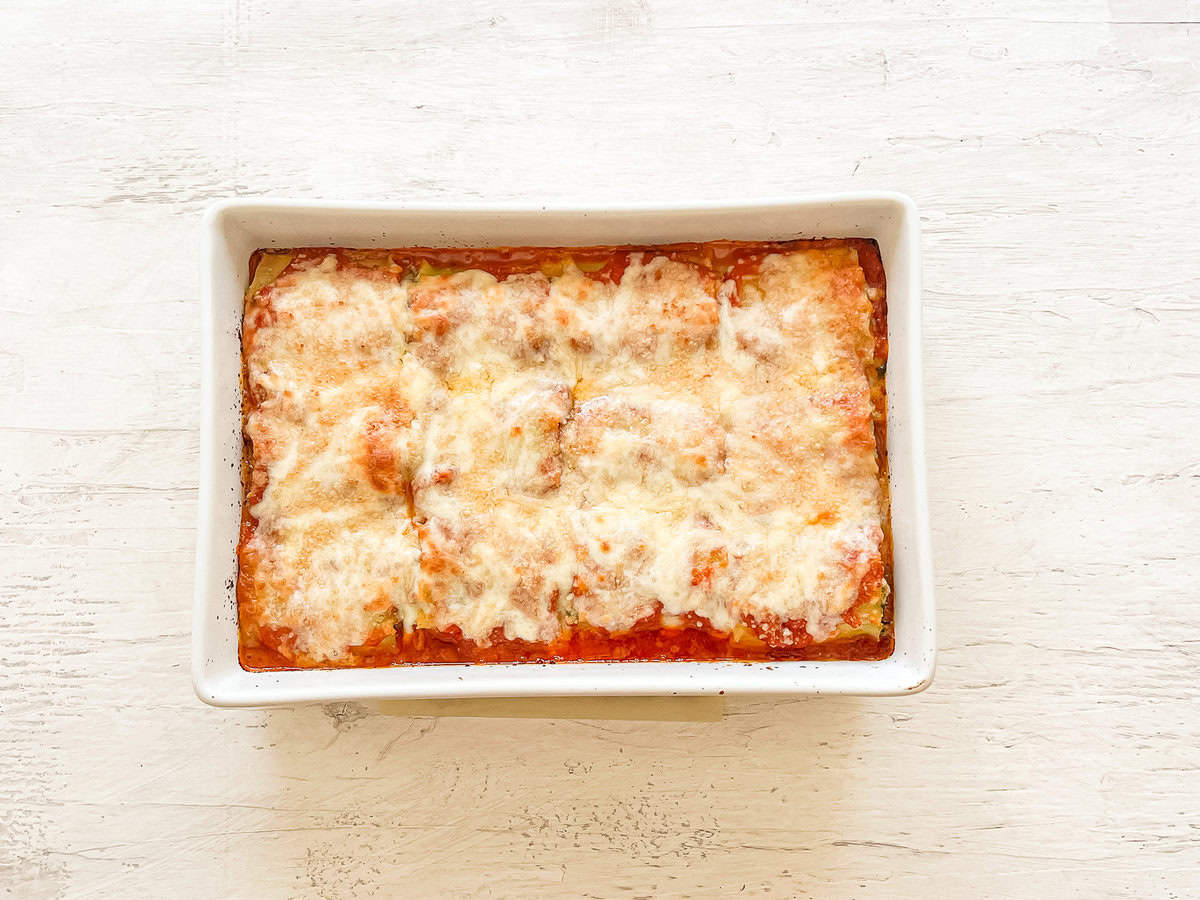 Spinach lasagna rolls in a white casserole dish just out of the oven.