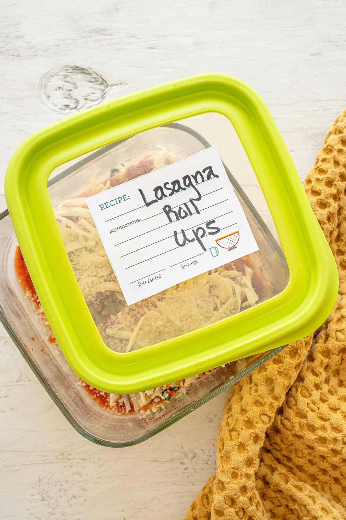 Spinach lasagna rolls in a glass baking dish with a label on the lid ready for the freezer.