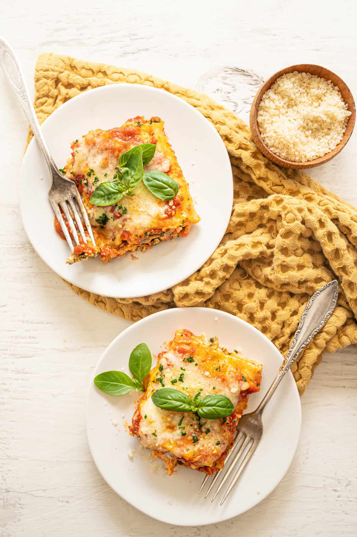 Two plates each with a single spinach lasagna roll-ups topped with fresh basil leaves.