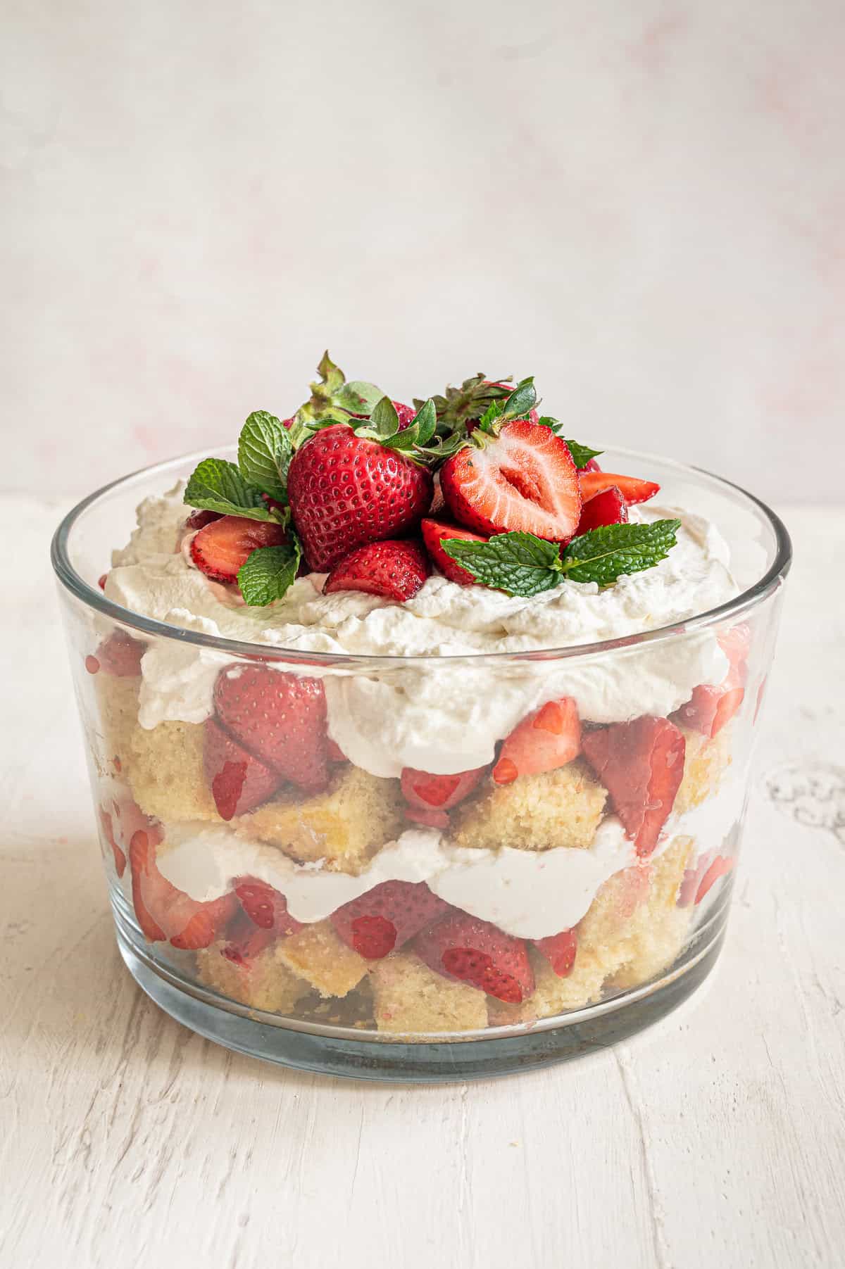 Strawberry shortcake trifle with whole and sliced strawberries and fresh mint leaves on top.