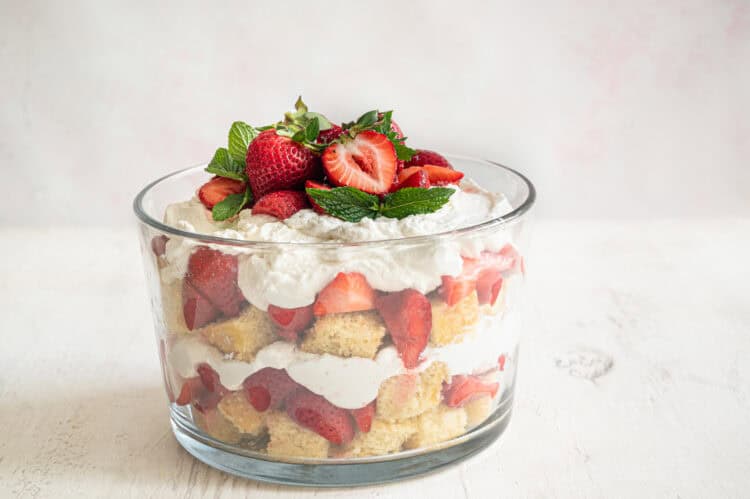 Strawberry shortcake trifle in a glass dish with strawberries and fresh mint leaves on top.