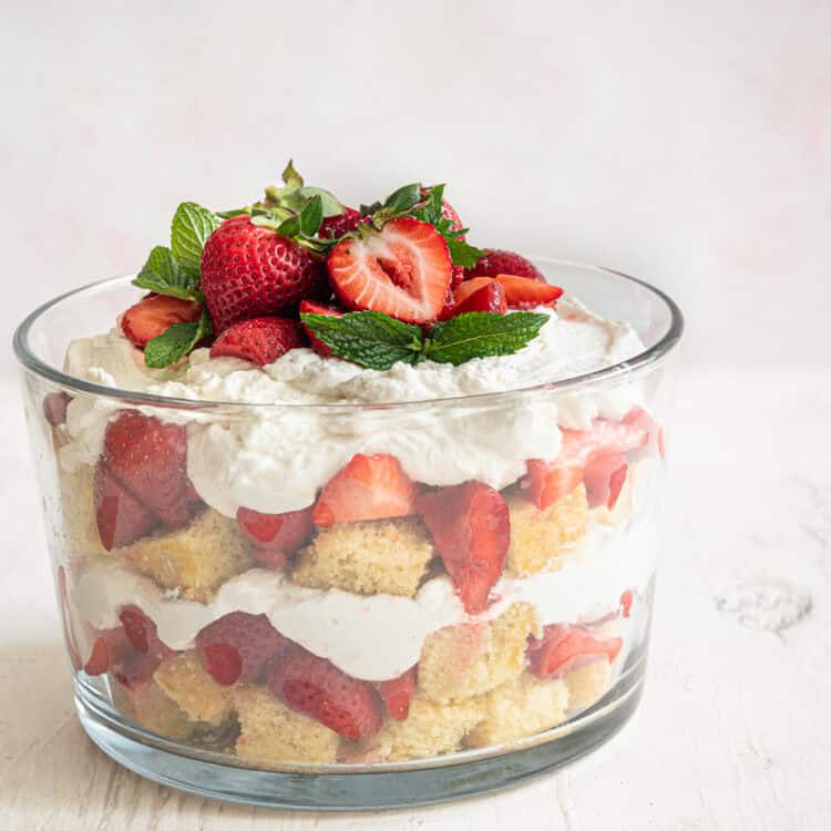 Strawberry shortcake trifle in a glass dish with strawberries and fresh mint leaves on top.