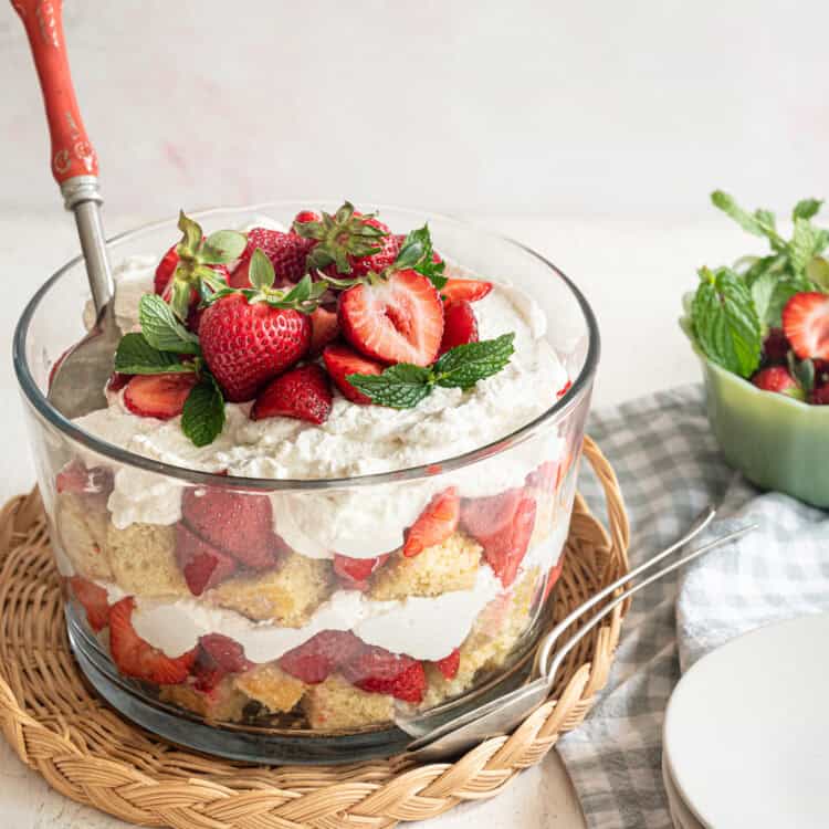 Strawberry shortcake trifle in a glass trifle dish with a serving spoon inside it.