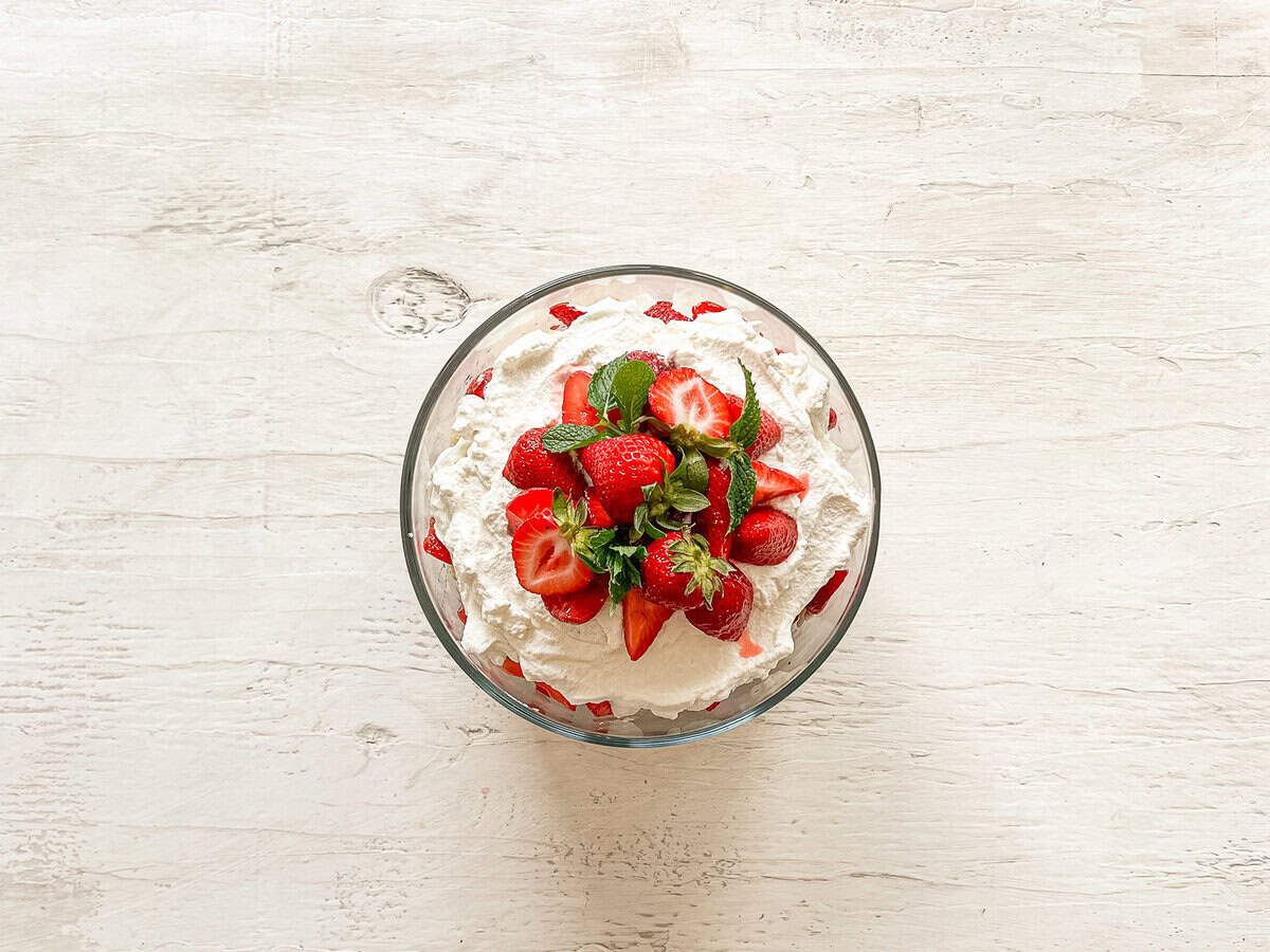 Strawberry shortcake trifle with fresh whipped cream, strawberries, and fresh mint leaves on top.