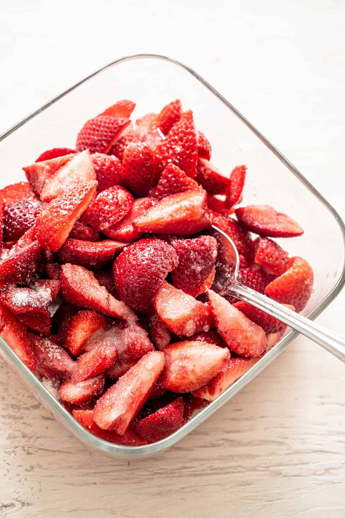 Sliced strawberries in a glass baking dish being tossed with sugar.