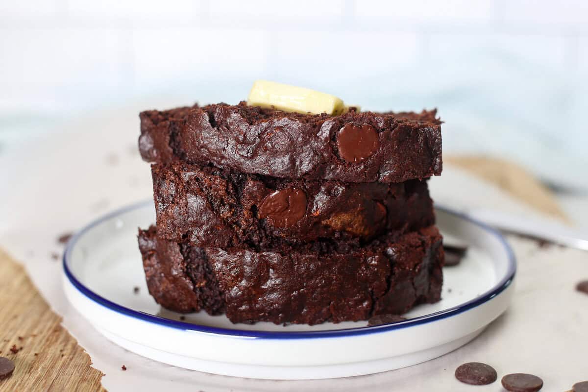 Three slices of double chocolate zucchini bread stacked up with a pat of butter on top.